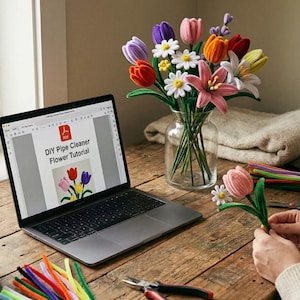 May include: A laptop displays a DIY pipe cleaner flower tutorial. A bouquet of colorful pipe cleaner flowers sits in a glass vase. A person is crafting a pink pipe cleaner tulip. Other craft supplies and plants are on the wooden table.