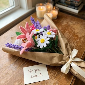 Pode incluir: Um buqu&ecirc; de flores artesanais embrulhado em papel pardo e amarrado com uma fita creme. O buqu&ecirc; inclui l&iacute;rios cor-de-rosa, margaridas brancas e lavanda roxa. Um pequeno cart&atilde;o diz "For You, Love, A."
