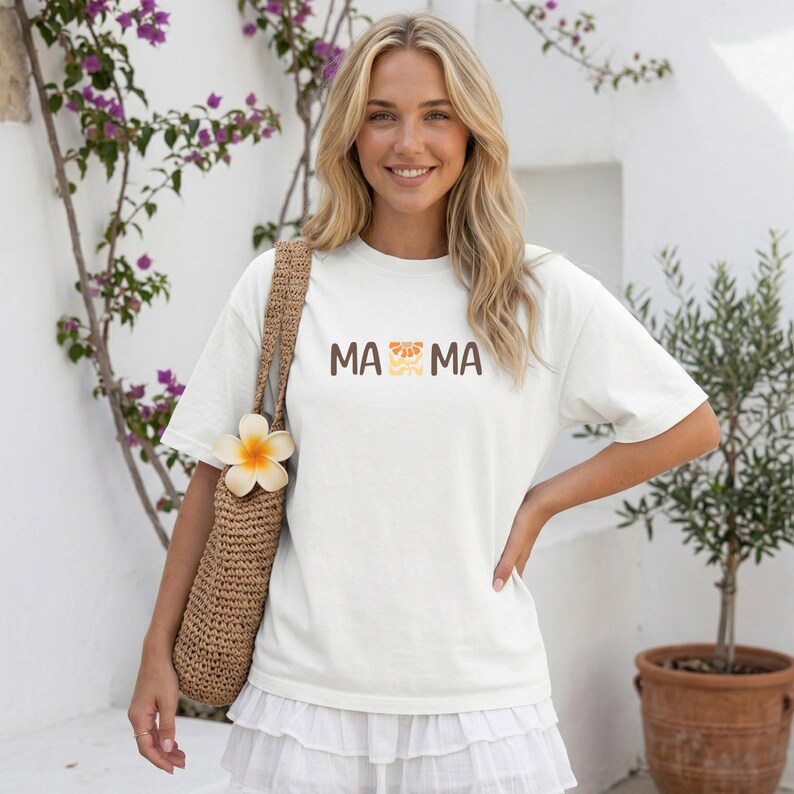 Woman wearing a white Comfort Colors mama shirt with brown MAMA lettering and a retro floral icon in orange, beige, and golden tones.