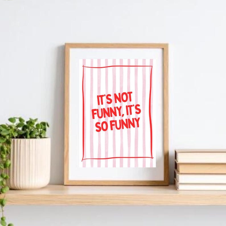 May include: Wooden framed print with the text "IT'S NOT FUNNY, IT'S SO FUNNY" in red. The print has a white background with pink vertical stripes and a red border. The frame is light brown.
