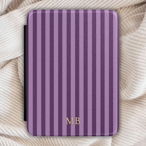 May include: A rectangular e-reader cover featuring a vertical striped pattern in alternating shades of light purple and dark purple. The cover has a textured surface and displays the gold-colored capital letters MB centered near the bottom edge.