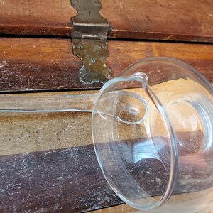 May include: A clear glass ladle with a long handle. The ladle is resting on a wooden surface.