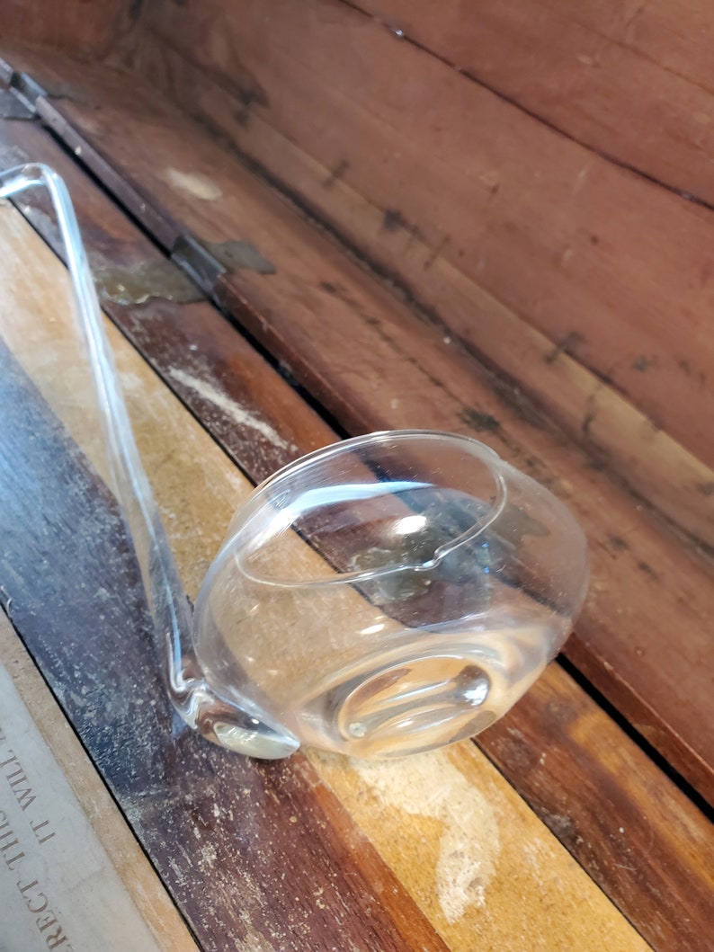 May include: A clear glass ladle with a long handle, resting on a wooden surface.