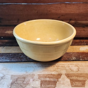 May include: A yellow ceramic mixing bowl with a smooth, glossy finish. The bowl has a rounded shape and a slightly flared rim.