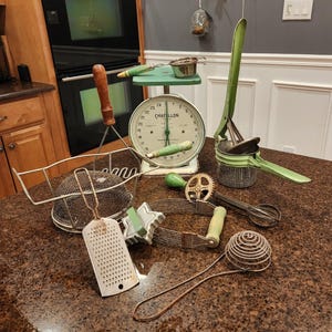 May include: A collection of vintage kitchen tools and gadgets, including a green potato ricer, a green and white scale with the brand name "Chatillon", a wire mesh strainer, a grater, a green and white cookie cutter, a wire whisk, and a wire egg separator.