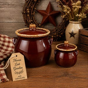 May include: Two dark brown ceramic pots with matching lids and side handles. Each pot features a decorative, textured rim with a speckled tan finish. A tan paper tag is attached, printed with the text: Never Lost Garden, sold individually.