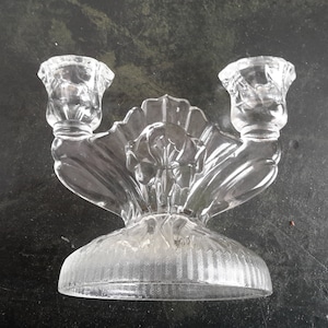 May include: A clear glass candle holder with two candle cups and a decorative floral design.