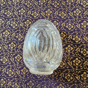 May include: A clear, egg-shaped glass paperweight featuring a series of vertical, raised ridges that extend from the top to the base. The glass surface is smooth and transparent, with the letters USA embossed clearly near the bottom edge.