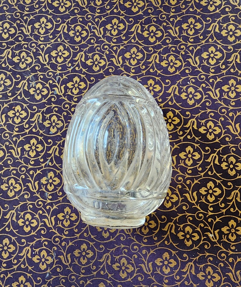 May include: A clear, egg-shaped glass paperweight featuring a series of vertical, raised ridges that extend from the top to the base. The glass surface is smooth and transparent, with the letters USA embossed clearly near the bottom edge.
