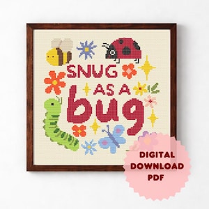 Peut inclure: Une broderie au point de croix encadrée en bois avec l'inscription "SNUG AS A bug" en rouge. Le motif comprend une abeille jaune, une coccinelle rouge, une chenille verte, des fleurs et des étoiles. Un autocollant rose indique "TÉLÉCHARGEMENT NUMÉRIQUE PDF".