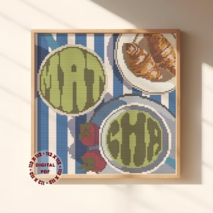 May include: A framed cross-stitch artwork featuring a whimsical food-themed design. The artwork includes the words "EAT" and "CHOMP" in green, stylized lettering, along with images of food on plates. The background has blue and white stripes.