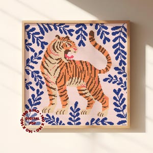 Könnte beinhalten: Ein Kreuzstichmuster mit einem orange-schwarzen Tiger mit offenem Maul auf hellrosa Hintergrund. Der Tiger ist von einem Rand aus dunkelblauen Blättern umgeben. Ein kreisförmiger Stempel in der Ecke zeigt 140 x 140 DIGITAL PDF.