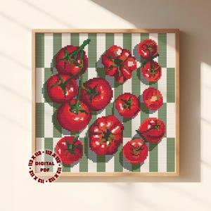 Op de afbeelding: Een digitaal PDF-kruissteekpatroon in een lijst met een verzameling rode tomaten met groene stelen, gerangschikt op een groen-witte gestreepte achtergrond. De lijst is lichtbruin. De tekst "112 x 112 DIGITAL PDF" staat in een cirkel linksonder.