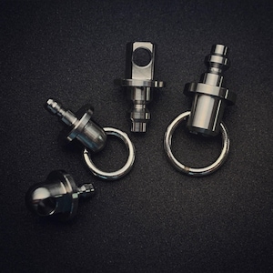 Può includere: Quattro portachiavi in metallo argentato con vari design. Ogni portachiavi ha un anello attaccato. I portachiavi hanno forme diverse, tra cui un design cilindrico, un design quadrato e un design a sfera. I portachiavi sono su una superficie nera.