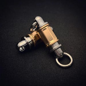 May include: Two cylindrical metal connectors featuring a central brass-toned body with vertical grooves and polished silver-toned end caps. Each connector includes a small circular metal ring attached to one end, designed for secure attachment.
