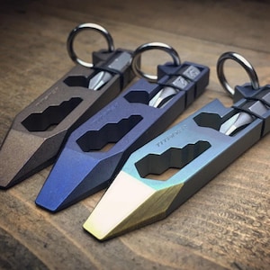 以下が含まれることがあります： 茶色、青、ターコイズ色の3つのマルチツール。それぞれにキーリングとドライバービットが付いています。ツールは幾何学的なデザインで、木製の表面に表示されています。「TITANIUM」の文字がツールの1つに表示されています。