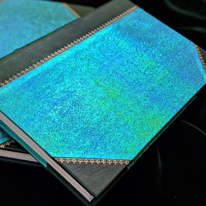 May include: A teal blue hardcover book with a gold decorative border. The book has a textured, iridescent cover.