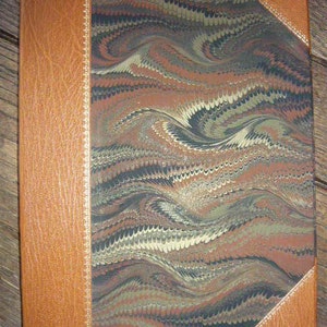 Puede incluir: Un diario encuadernado en cuero marr&oacute;n con una cubierta de m&aacute;rmol que presenta un patr&oacute;n de remolino de negro, marr&oacute;n y blanco. La cubierta tiene un borde decorativo a lo largo de los bordes.