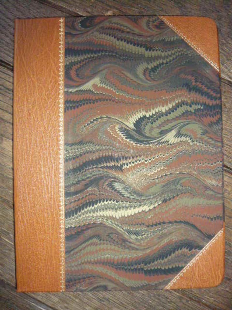 Puede incluir: Un diario encuadernado en cuero marr&oacute;n con una cubierta de m&aacute;rmol que presenta un patr&oacute;n de remolino de negro, marr&oacute;n y blanco. La cubierta tiene un borde decorativo a lo largo de los bordes.