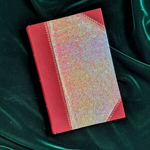 May include: A red leather-bound journal with a gold-embossed design and a glittery iridescent cover.