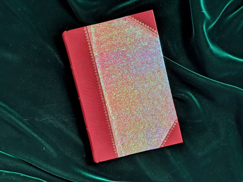 May include: A red leather-bound journal with a gold-embossed design and a glittery iridescent cover.