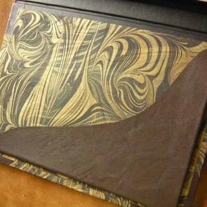 Puede incluir: Un diario encuadernado en cuero marr&oacute;n con una cubierta de papel marmoleado. La cubierta presenta un patr&oacute;n de remolino de oro y marr&oacute;n.