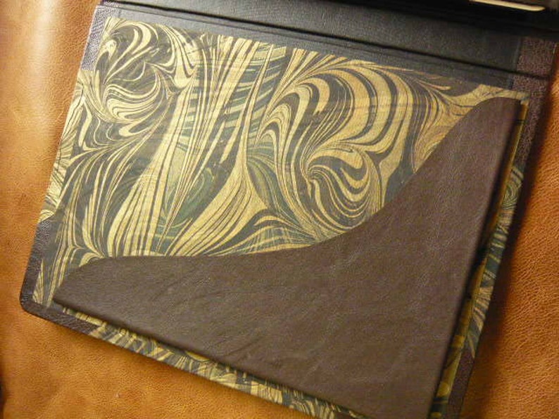 Puede incluir: Un diario encuadernado en cuero marr&oacute;n con una cubierta de papel marmoleado. La cubierta presenta un patr&oacute;n de remolino de oro y marr&oacute;n.