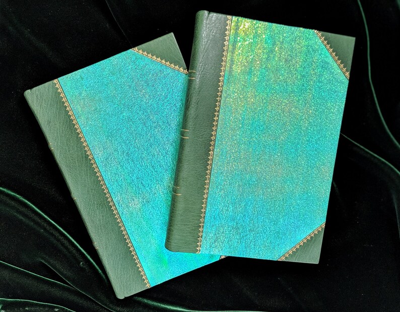 May include: Two green leather-bound journals with a teal iridescent cover. The journals have gold accents and are closed.