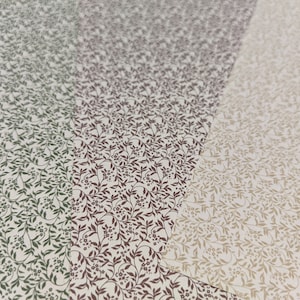 May include: Three sheets of paper with a repeating pattern of small, dark green, burgundy, and beige leaves and flowers on a white background.