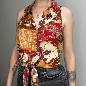 Puede incluir: Top sin mangas con cuello y diseño patchwork vibrante. El top presenta una mezcla de estampados florales y abstractos en tonos rojos, marrones, crema y dorados. Está atado a la cintura, creando una silueta favorecedora.