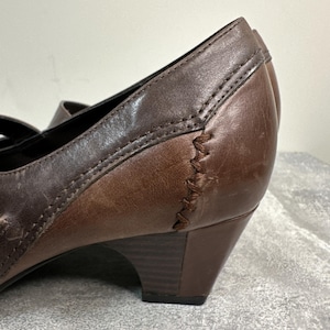 Może przedstawiać: Zbliżenie brązowego sk&oacute;rzanego buta z małym obcasem. But ma przeszyty wz&oacute;r z boku i pasek. Sk&oacute;ra ma postarzany wygląd z odcieniami.