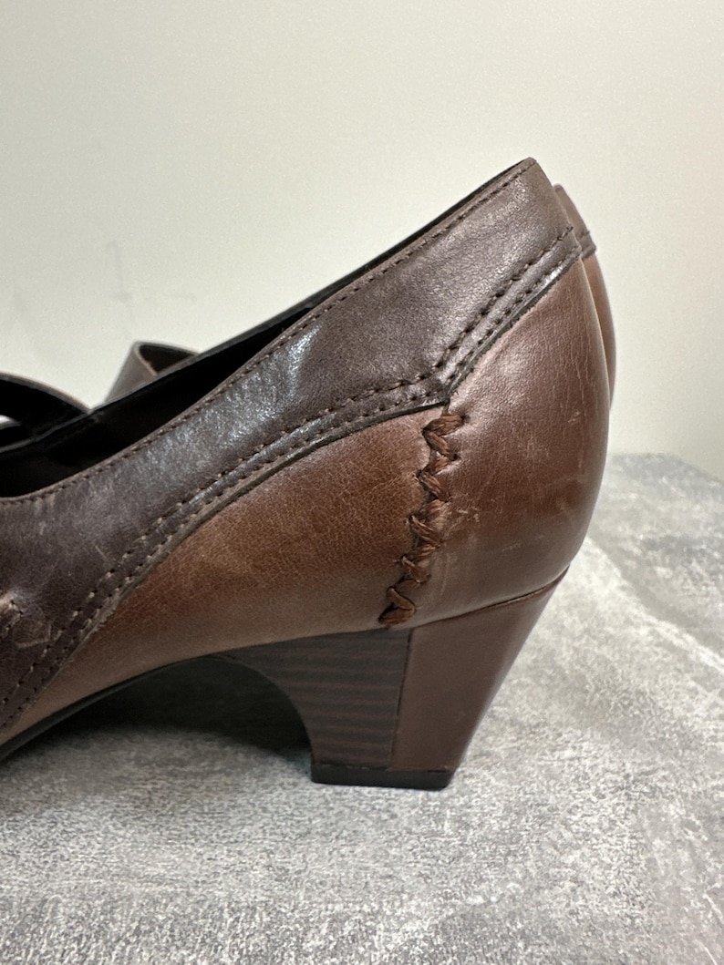 Może przedstawiać: Zbliżenie brązowego sk&oacute;rzanego buta z małym obcasem. But ma przeszyty wz&oacute;r z boku i pasek. Sk&oacute;ra ma postarzany wygląd z odcieniami.