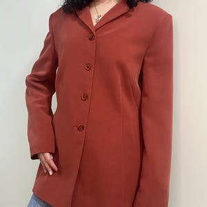 Puede incluir: Una taza de cerámica blanca con un asa negra y el texto "But First, Coffee" en negro y negrita. La taza está sobre una superficie de madera.