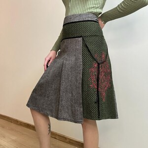 May include: A-line skirt with a unique design. The skirt features a gray panel on the left and a green patterned panel on the right, with a red floral design. The waistband is green with a black trim.
