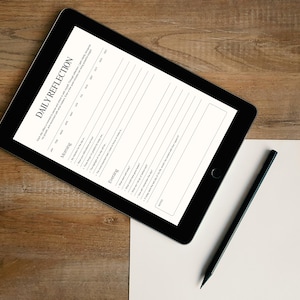 May include: A black tablet displaying a digital Daily Reflection planner template with sections for morning and evening prompts, accompanied by a black pencil resting on a blank white sheet of paper, all arranged on a wooden surface.