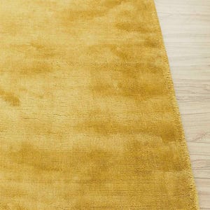Puede incluir: Alfombra de color amarillo mostaza con una superficie suave y texturizada. La alfombra rectangular tiene un aspecto afelpado, adecuada para una sala de estar o un dormitorio. El color de la alfombra es un tono c&aacute;lido y acogedor.