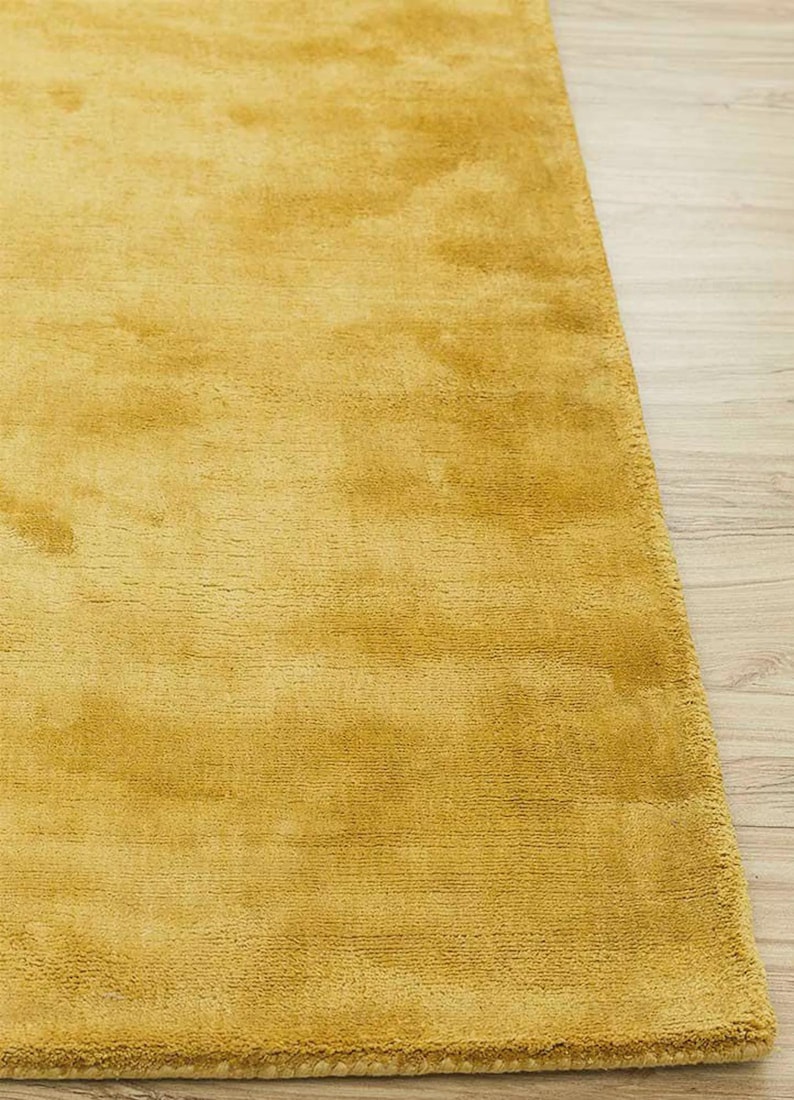 Puede incluir: Alfombra de color amarillo mostaza con una superficie suave y texturizada. La alfombra rectangular tiene un aspecto afelpado, adecuada para una sala de estar o un dormitorio. El color de la alfombra es un tono c&aacute;lido y acogedor.
