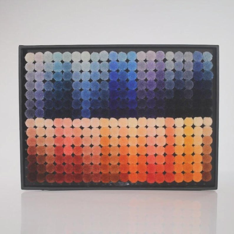 Pode incluir: Obra de arte abstrata com um gradiente de cores. A obra &eacute; composta por pequenos tufos circulares dispostos em fileiras, que transitam de laranjas e vermelhos quentes na parte inferior para azuis e roxos frios na parte superior, tudo dentro de uma moldura preta.