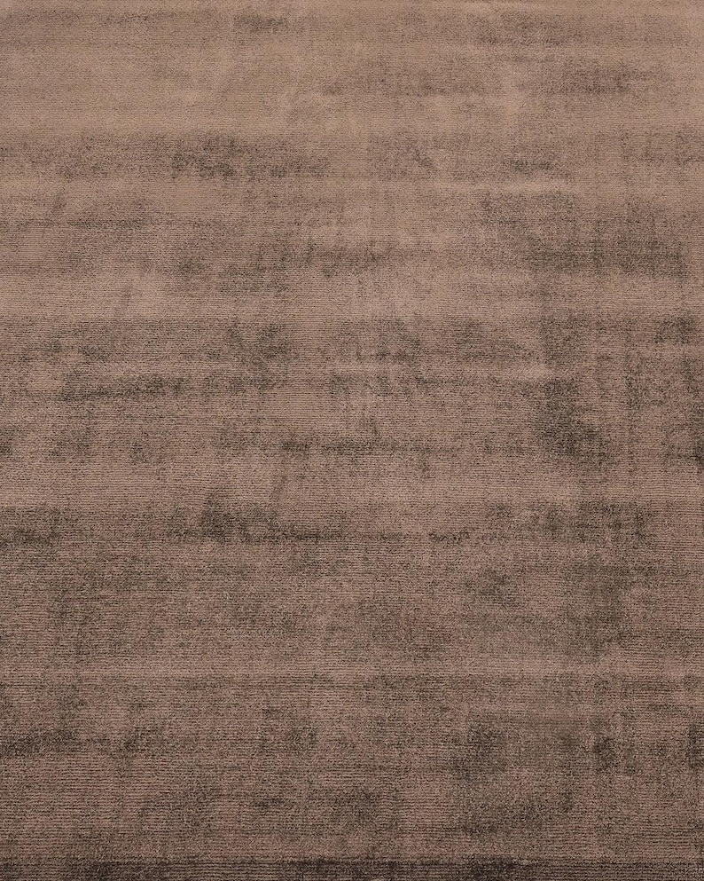 Pode incluir: Uma vista de perto de um tapete retangular grande. O tapete tem uma textura macia e felpuda e uma cor rosa empoeirado suave com &aacute;reas mais escuras e manchadas. O design apresenta estrias horizontais, criando um padr&atilde;o sutil e texturizado. O tapete parece ser feito de um material macio.