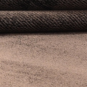 Pode incluir: Close-up de um tecido texturizado castanho. O material tem uma apar&ecirc;ncia tecida com um padr&atilde;o subtil. A imagem mostra o tecido dobrado sobre si mesmo, revelando sua textura e profundidade. Ideal para estofados ou projetos t&ecirc;xteis.