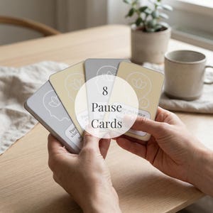 Puede incluir: Una mano sostiene una baraja de ocho "Pause Cards" en amarillo claro y gris. Cada carta presenta un diseño facial minimalista y la palabra "Pause". Las cartas están sobre una mesa de madera, con una taza y una planta en el fondo.
