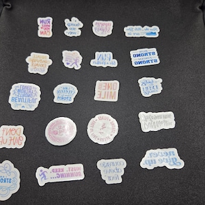 May include: A collection of motivational stickers with various phrases and designs. The stickers are white with colorful text and graphics, including phrases like "Run," "Strong," and "One Mile." The stickers are arranged on a dark surface.