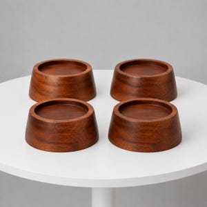 Puede incluir: Un juego de cuatro posavasos circulares de madera con un acabado suave de color marrón oscuro y patrones de veta de madera visibles. Cada posavasos presenta un perfil lateral ligeramente cónico y un centro rebajado con base plana.