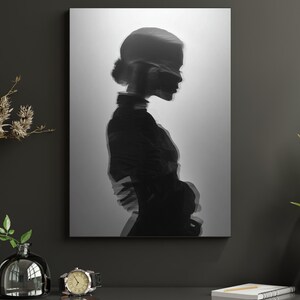 May include: Monochrome art print depicting a woman's profile with a layered, blurred effect. The artwork is mounted on a wall, creating a minimalist look. The woman's hair is in a bun, and she wears a high-necked top.