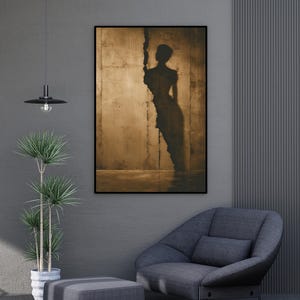 May include: A framed artwork featuring a silhouette of a person against a textured, sepia-toned background. The artwork is in a black frame, and the room has a modern aesthetic with a gray color scheme. A gray armchair and ottoman are in the foreground.