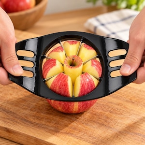 Pode incluir: Um cortador de maçãs de plástico preto com lâminas de aço inoxidável, concebido com duas pegas laterais ergonómicas com três ranhuras cada. A ferramenta é posicionada sobre uma maçã vermelha e amarela, dividindo o fruto em oito gomos.