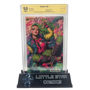 Puede incluir: Un cómic de Batman #108 calificado, en un estuche protector, sobre un soporte negro. El cómic presenta un personaje con cabello verde y ropa colorida. El soporte tiene el texto "LITTLE STAR COMICS".