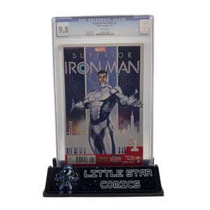 以下が含まれることがあります： 保護ホルダーに収められた、Superior Iron Man #1の評価済みコミック。表紙には、銀と白のスーツを着たアイアンマンが描かれています。コミックは、「LITTLE STAR COMICS」の文字が入った黒いスタンドに表示されています。