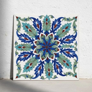 May include: A square ceramic tile featuring a symmetrical floral mandala pattern in shades of deep blue, turquoise, sage green, and dark red against a white background. The design consists of repeating leaf-like motifs radiating from the center.