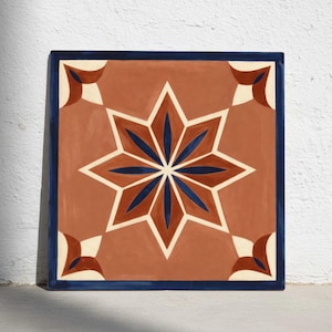Puede incluir: Azulejo cuadrado de terracota con un diseño de estrella en el centro. La estrella presenta detalles azules y crema. El azulejo tiene un borde azul oscuro. Mide aproximadamente 30 cm x 30 cm y se usa para decoración del hogar.